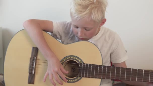 The blonde boy learns to play the guitar at home — Stock Video