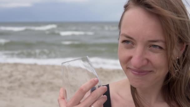 한 아름다운 여인 이 바다 옆의 유리잔에서 와인을 마시며 즐겁게 웃는다 — 비디오