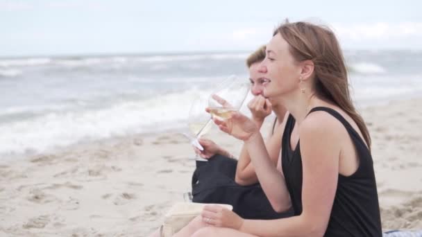 Летом подруги пьют вино на пляже у моря и весело смеются — стоковое видео