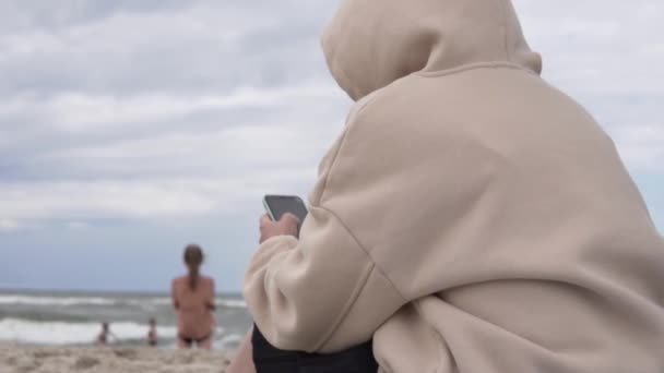 Un message de type femme sur un téléphone portable sur la plage au bord de la mer tout en marchant avec les enfants — Video