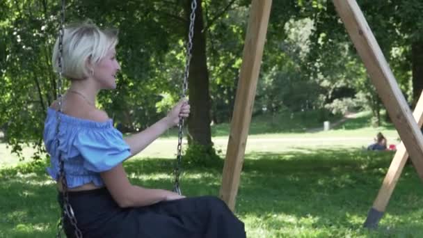 Güzel sarışın bir kadın yazın parkta salıncakta sallanıyor. — Stok video