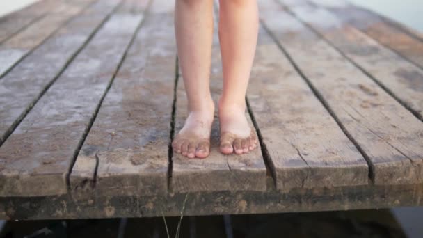 Дитячі ноги м'яко ходять по дерев'яному мосту біля води влітку — стокове відео