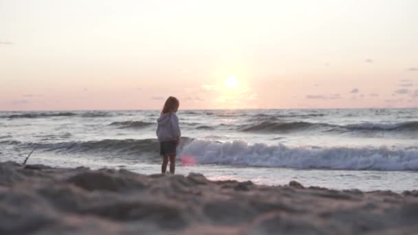 Mała dziewczynka na opuszczonej piaszczystej plaży ogląda zachód słońca w morzu — Wideo stockowe