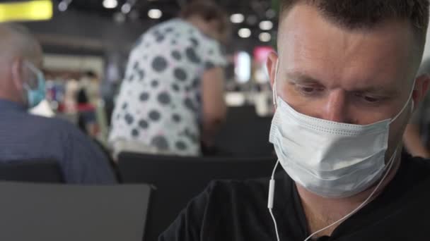Zbliżenie, mężczyzna w masce medycznej i słuchawki czeka na lot na lotnisku, — Wideo stockowe