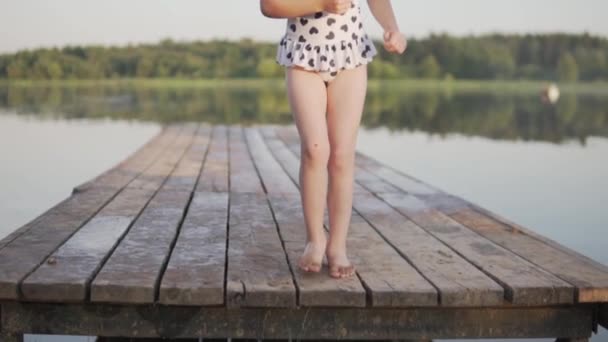 Die Beine eines kleinen Mädchens auf einer Holzbrücke am See im Sommer — Stockvideo