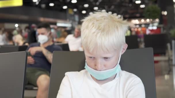 En pojke som bär en Medina mask i ansiktet sitter i flygplatsloungen under coronavirus pandemin — Stockvideo