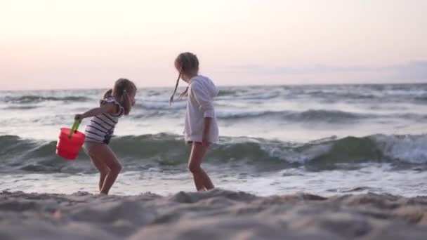 İki küçük kız gün batımında kumlu bir sahilde oynuyorlar. — Stok video