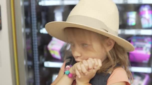 Een klein meisje met een hoed vraagt om een speeltje in de winkel, een close-up — Stockvideo