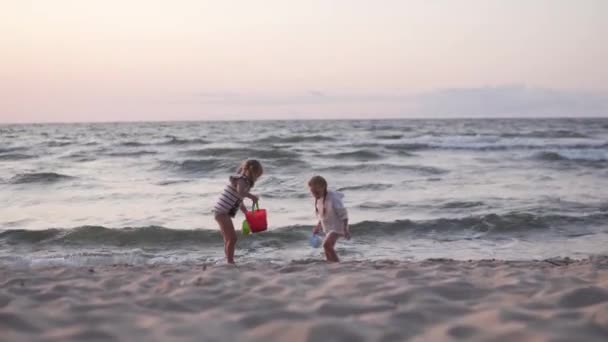 İki kız kardeş yazın gün batımında deniz kenarında plaj oyuncakları oynarlar. — Stok video