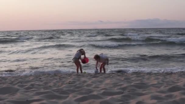 Dua gadis kecil bermain di pantai saat matahari terbenam di musim panas — Stok Video