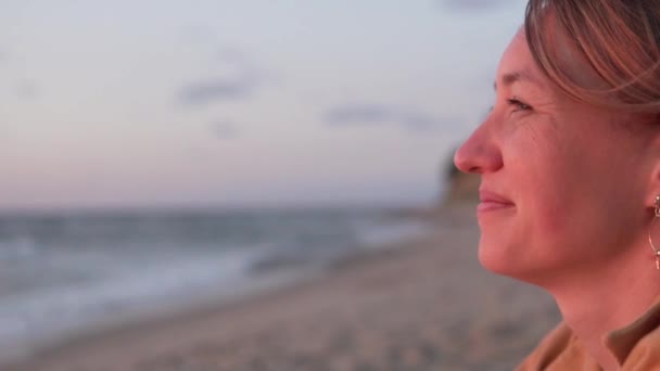 Κοντινό πλάνο, μια όμορφη γυναίκα που βλέπει το ηλιοβασίλεμα στη θάλασσα — Αρχείο Βίντεο