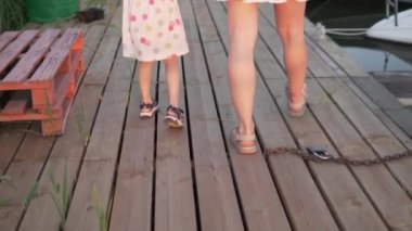 Yakın plan, anne ve kız yazın teknelerin yanından geçen ahşap bir köprü boyunca yürür.