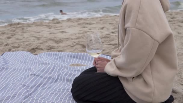Una hermosa mujer bebe vino junto al mar en la playa en otoño — Vídeos de Stock