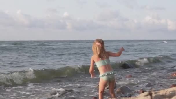 Zabawne dziecko w stroju kąpielowym stoi nad morzem i nie ośmiela się wejść do zimnej wody — Wideo stockowe