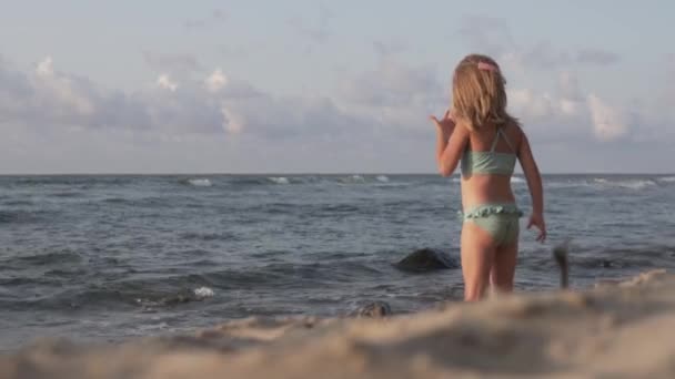 Krásná holčička v plavkách stojí na pláži u moře — Stock video