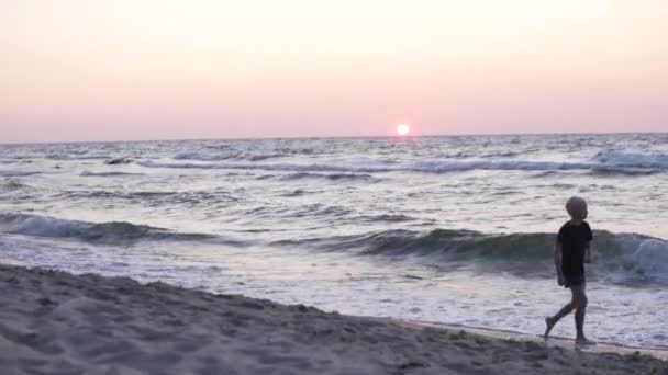 Мальчик быстро ходит по пляжу на закате летом — стоковое видео