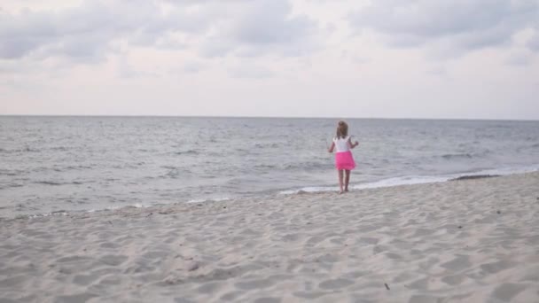 Una bambina cammina lungo la spiaggia in riva al mare la sera. — Video Stock