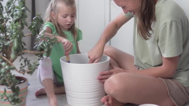 Seorang ibu dan seorang putri kecil menanam tanaman rumah tangga ke dalam panci besar rumah — Stok Video