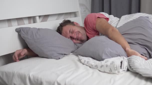 Un hombre sonríe mientras duerme por la mañana. Un hombre guapo se despierta de buen humor — Vídeo de stock