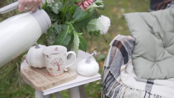 Forró tea öntött egy csésze termoszt az őszi parkban az asztalon a pad mellett. őszi kávézó Halloweenkor — Stock videók