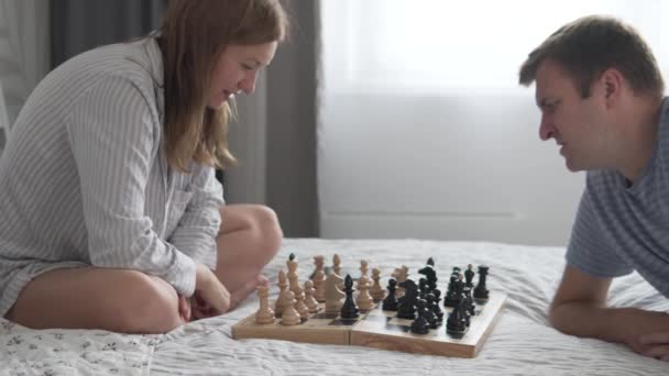 Ein hartnäckiger Kampf, ein Mann und eine Frau spielen zu Hause auf dem Bett Schach — Stockvideo