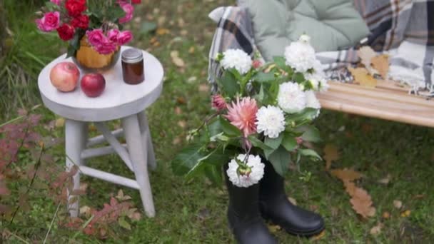 Bahçe arazisinde sonbahar dekoru, sıcak battaniyeli bir bank ve bahçeden gelen çiçeklerle dolu bir masa. — Stok video