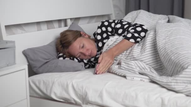 En vacker kvinna använder en mobiltelefon på morgonen i sängen — Stockvideo