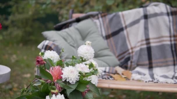 Bank in de vaste tuin met een warme deken en een tafel met boeketten bloemen uit de tuin. — Stockvideo