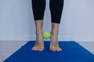 Ayaklara yakın çekim, kadın ayak jimnastiği yapıyor yoga minderinde tenis topu, yakın çekim ploan