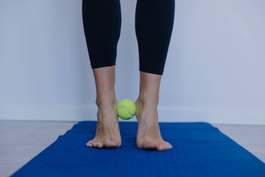 Çıplak ayaklar, ayak parmaklarının altında tenis topuyla dengede durmak, ayak hareketliliği egzersizi, plantar rahatlama, ince ince