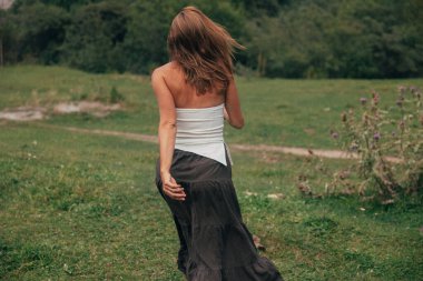 Kafkasyalı bir kadın vadide yürüyor. Dalgalı etekle keşif modunda. Uzak tepeler.,