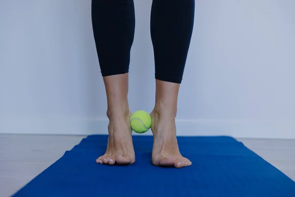 Çıplak ayaklar, ayak parmaklarının altında tenis topuyla dengede durmak, ayak hareketliliği egzersizi, plantar rahatlama, ince ince