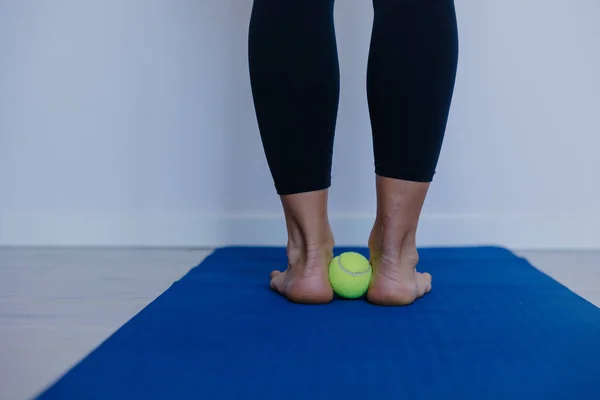 Ayak kemerinin altında tenis topuna basan ayak, yoga minderinde duran, ağırlık değiştiren kişi.