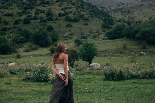 Kafkasyalı kadın vadide gözcülük yapıyor, elleri arkada dalgın dalgın duruyor, panoramik yeşil manzaralı.,