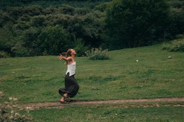 Çimenli tepede yürüyen bir kadın, yeşil çayırlarda kaygısızca gezinen beyaz etekli, siyah kollu bir kadın.