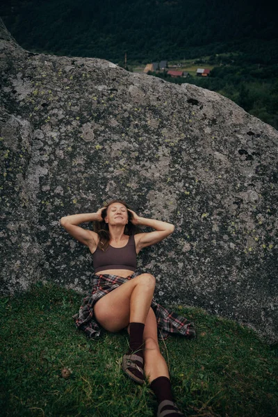 Kafkasyalı rahat bir kadın yamaçta yaslanıyor, bohem bir dinlenme, açık bir duruş, sıcak bir ruh hali.