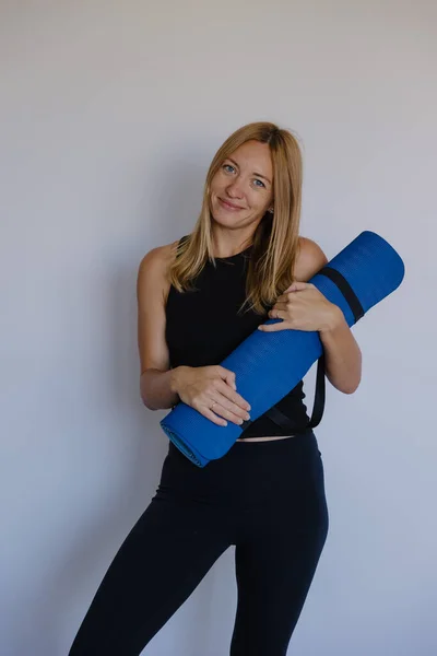 Kafkasyalı eğitmen yoga minderini kucaklıyor. Yumuşak gülüş. Rahat duruş.