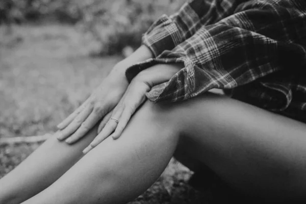 Eller dizlerin üzerinde, ekose gömlek, çıplak bacaklar çimenlerin üzerinde dinleniyor, tek renkli doku ve yumuşak doğal ışık.,