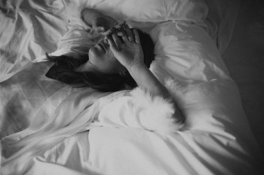 Kadın yatakta uzanıyor, sabah ışığı, yazar bitkin, kırışık çarşaflar, el üstünde alnı, tek renkli film tahılları.,