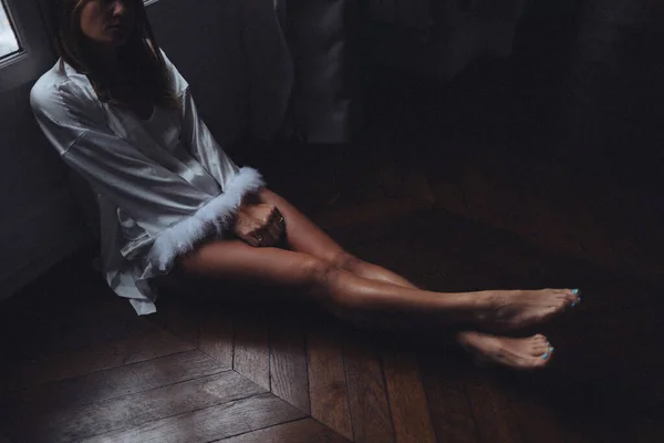 Hafifmeşrep kadın, yerde uzanmış ayakları üzerinde, parke üzerinde yalınayak, ipek bornoz örtülü, dalgın.