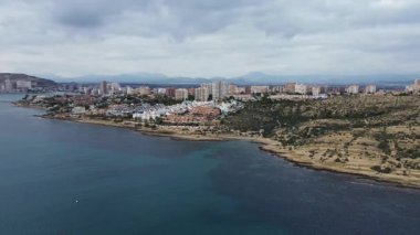 İspanya 'nın Alicante kentindeki Cabo de las Huertas kayalık burnu üzerinde uçan hava aracı görüntüleri, Akdeniz ve kıyı evleri görüş alanımızda. Berrak mavi suları birleştiren manzaralı bir kıyı manzarası.