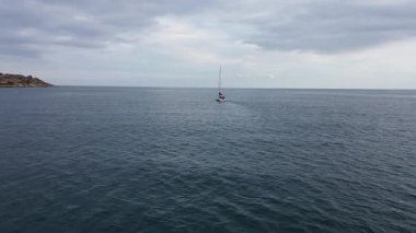 İnsansız hava aracı, İspanya 'nın Alicante kenti yakınlarındaki sakin Akdeniz sularında seyreden bir yatı takip ediyor. Uzakta kayalık bir sahil şeridi var..