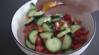 Bir kadın bir kase doğranmış sebzenin üzerine taze limon suyu sıkıyor ve sağlıklı ev yapımı salataya taze narenciye tadı katıyor. Mutfakta salatalık ve domates salatası hazırlamaya yakın çekim..