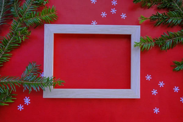 White picture frame on red background with tinsel, and christmas tree branches. Christmas postcard top view. Copy space