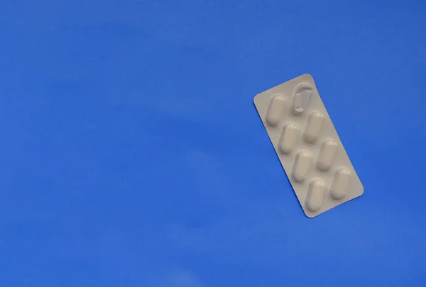White packaging with pills across blue background. Healthcare concept. Top view. Treatment.
