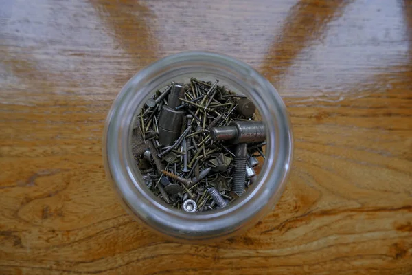 close up of metallic nails, peds, studs, pin in glass jar on wooden table top view. Industrial tools.