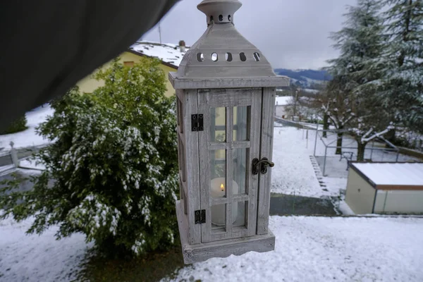 hand holding white wooden lantern with candle across winter landscape and backyard. Traditional. Holiday. Christmas