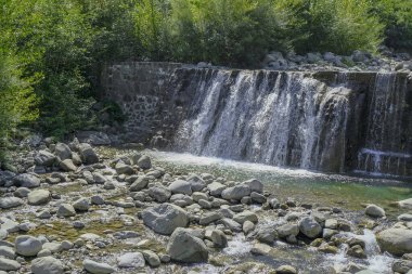 Ormanın karşısındaki dağlarda kayalıkları olan bir şelale. Doğal arkaplan 