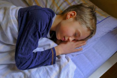 Mavi pijamalı tatlı sarışın çocuk, yakın plan yatakta uyuyor. Çocukların odası..