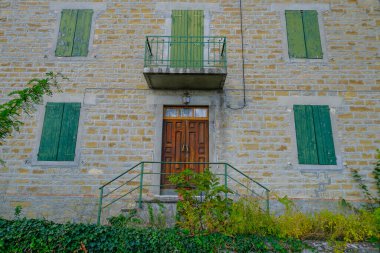 Yeşil kepenkleri, ahşap ana kapısı ve balkonu olan eski gri evin ön cephesi. Mimarlık. Avrupa.